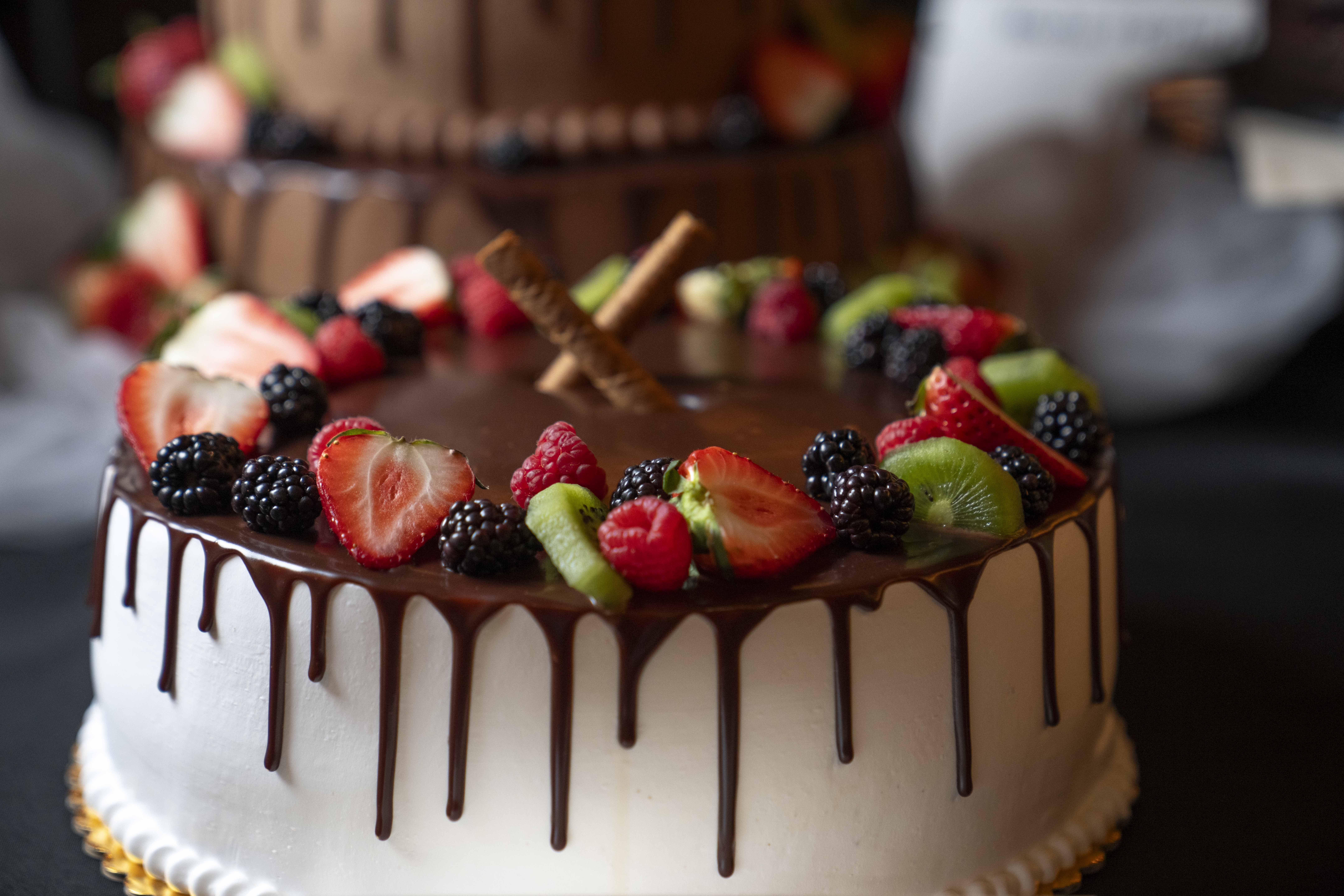 Close-up of a white cake with chocolate drips and fruit.