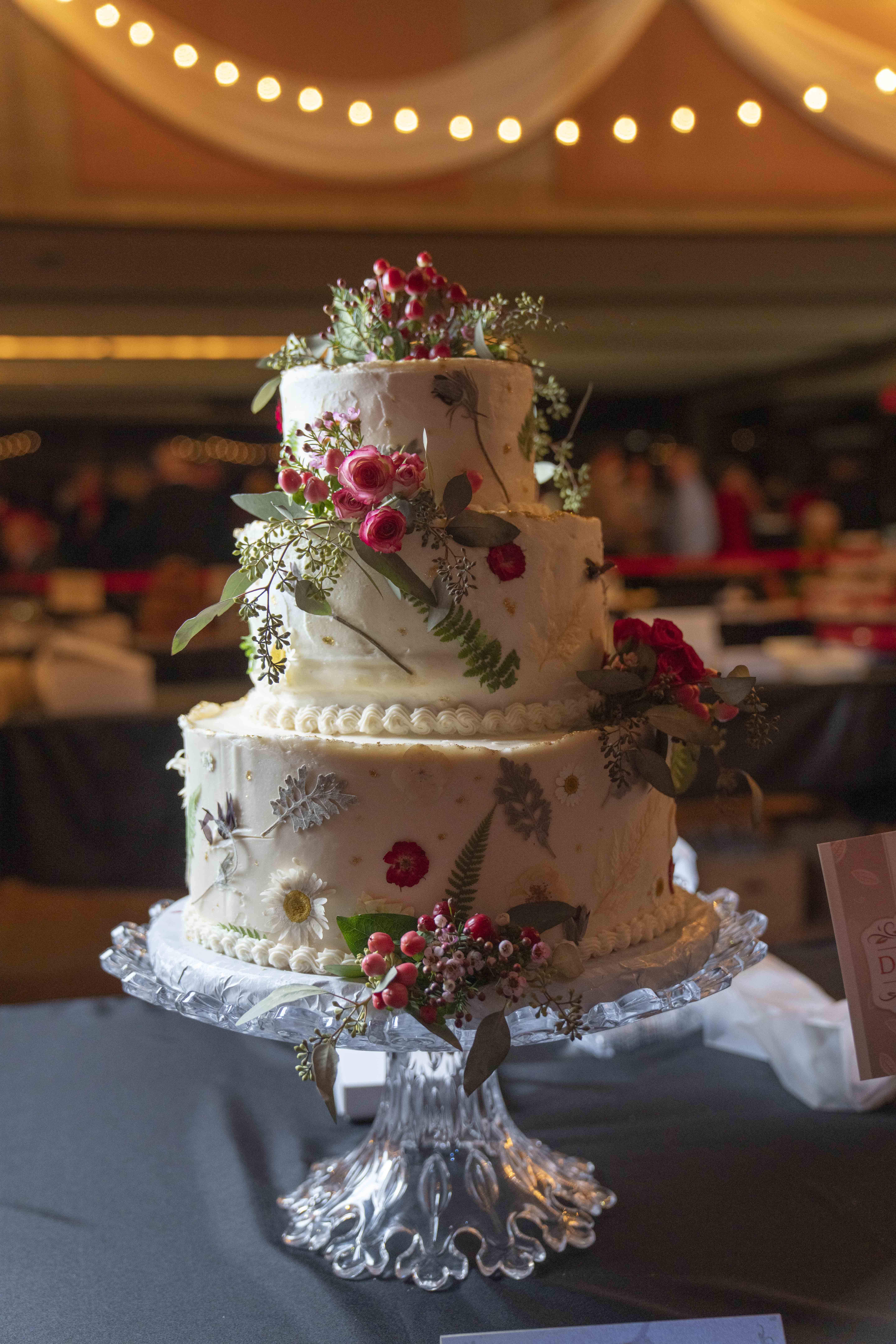 Three-tiered white cake decorated with floral detailing on an acrylic cake stand.