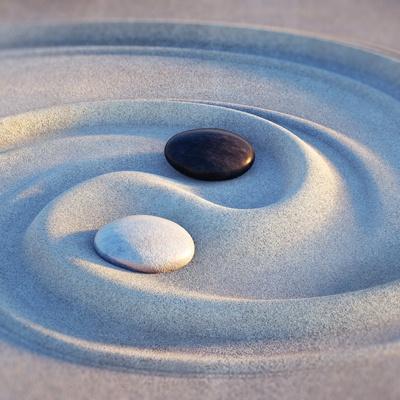 a black and a white stone in sand, arranged to represent a yin yang
